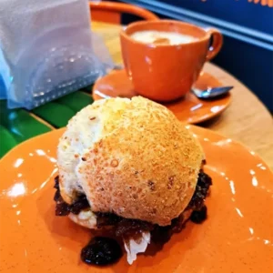 um pão de queijo recheado com cebolas caramelizadas da Liam Foods, e um capuccino, ao fundo